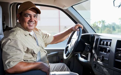 A man driving a work van, smiling.