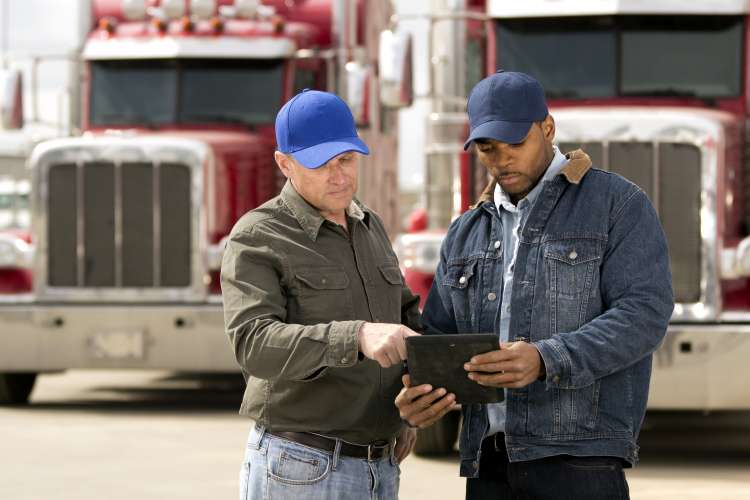 Two men standing in front of a fleet of trucks looking at a tablet.